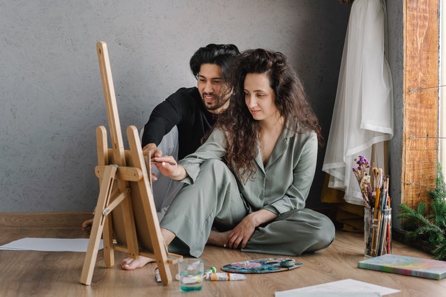 Couple sitting on the living room floor painting on a small easel.