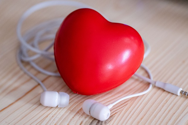 Photo of a red heart-shaped stress ball on a wooden table with small headphones.