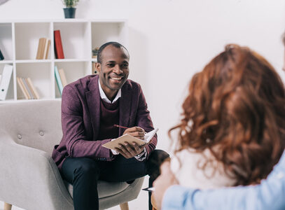 Photo of a man of color with a notebook talking to a couple in a white office.