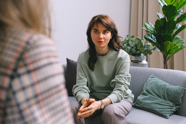Young woman in consultation sitting on a grey canaper with a plant in the background.