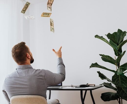 Photo of a man sitting at his desk from behind, tossing silver bills in the air.